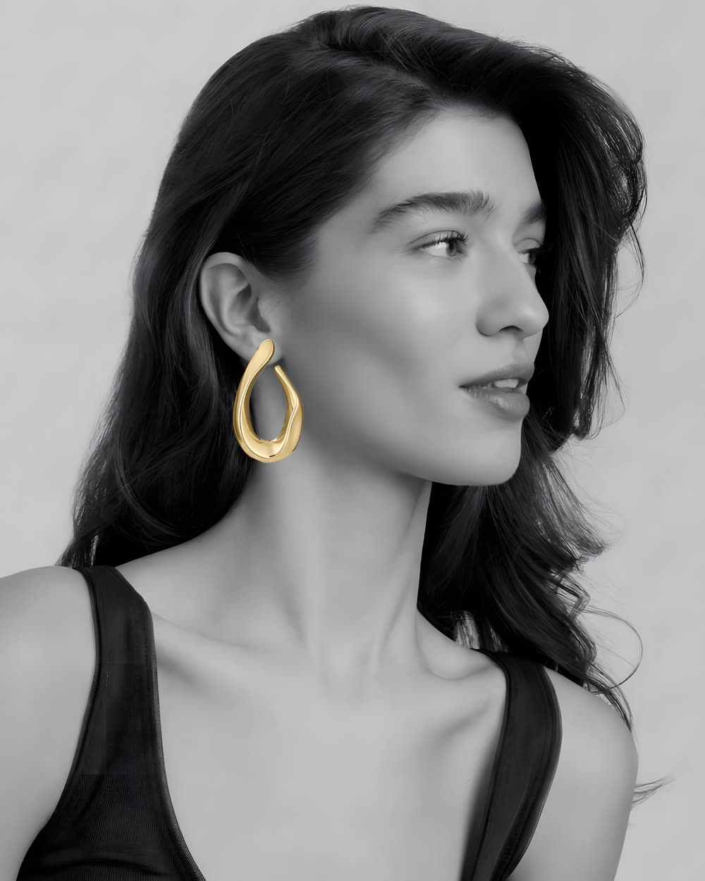 Mujer de perfil con el pelo recogido y un pendiente dorado de lágrima, en blanco y negro