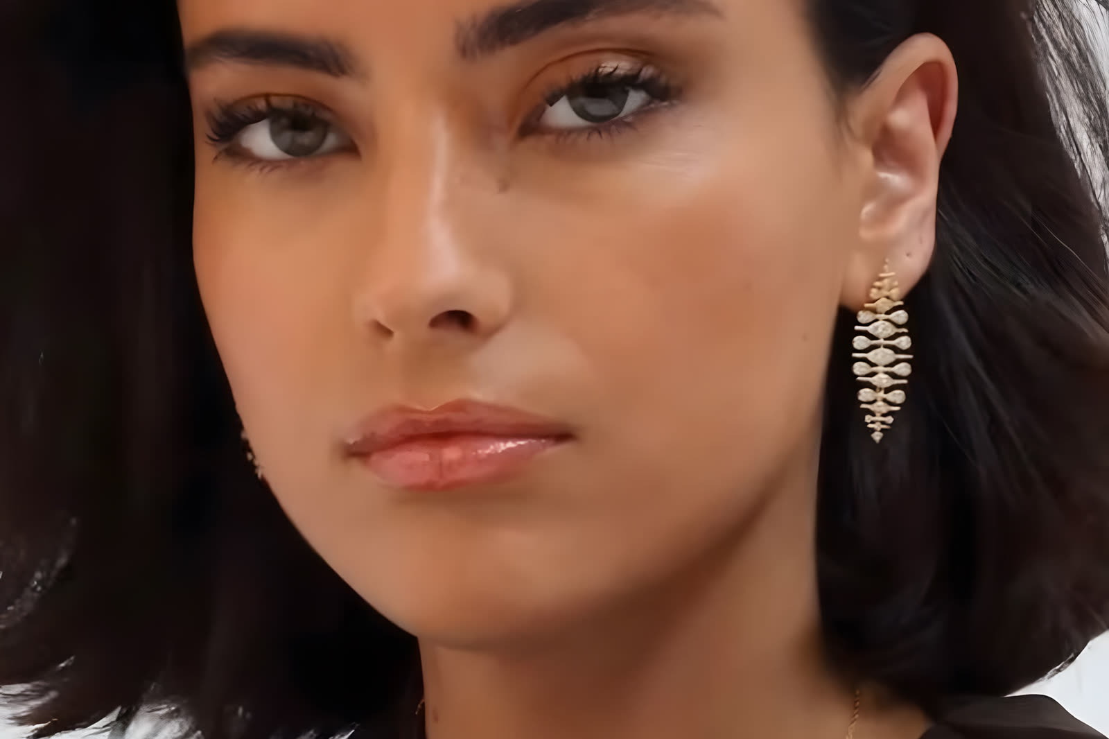 Pendiente largo dorado de circonitas en la oreja de una modelo